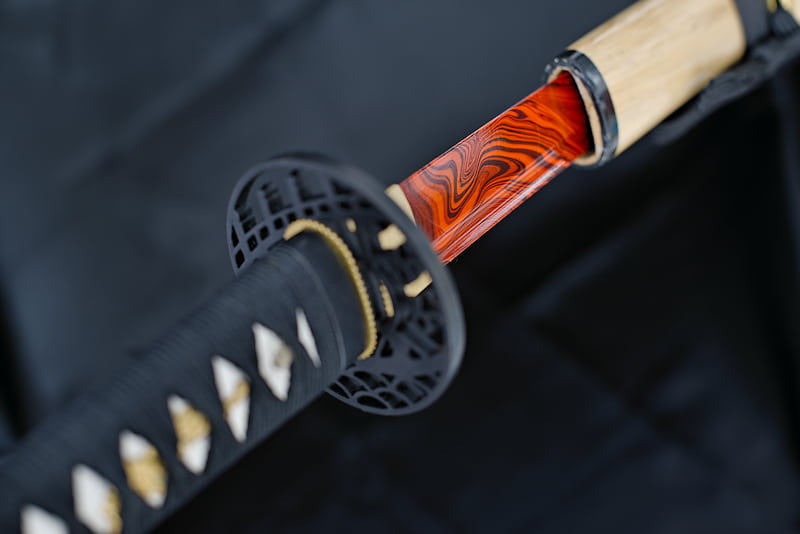 Katana tranchant, lame peinte en rouge et noir, avec fourreau (saya 鞘) en bois naturel laqué, sageo (下緒) et tsuka-Ito (柄糸) noirs | Certaines personnes cherchent leur raison d’être toute leur vie. D’autres explorent, la trouvent et suivent leur chemin dans l’harmonie.